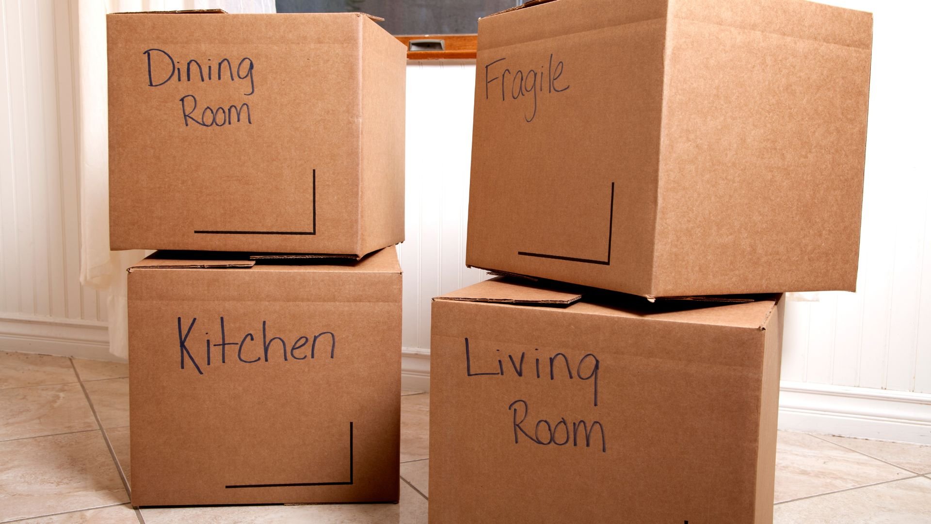 Moving boxes labeled with different room names stacked on floor