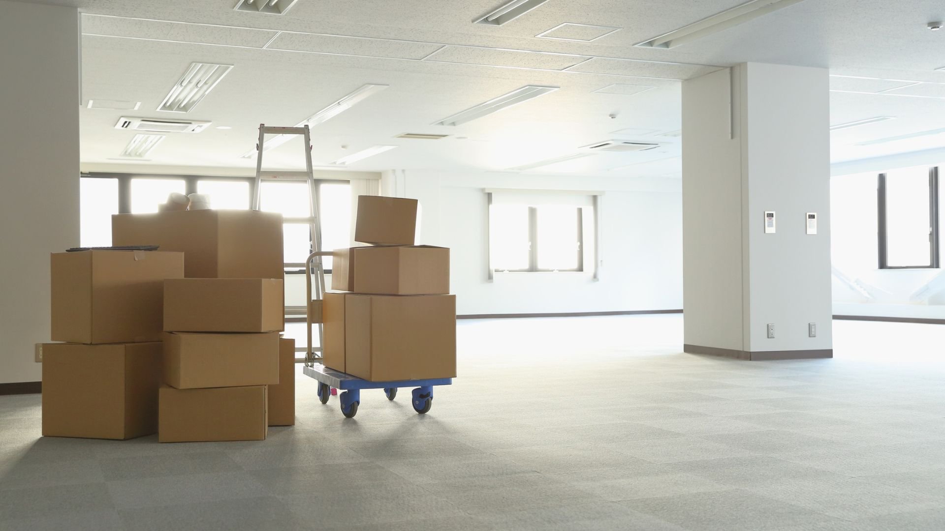 Moving boxes and hand truck in empty office space with ladder