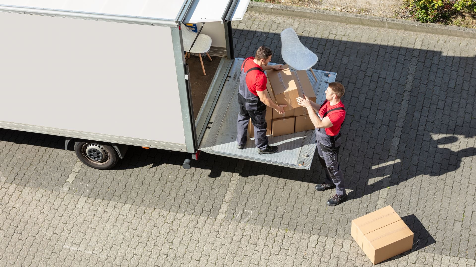 Two delivery workers loading cardboard boxes into a white delivery van