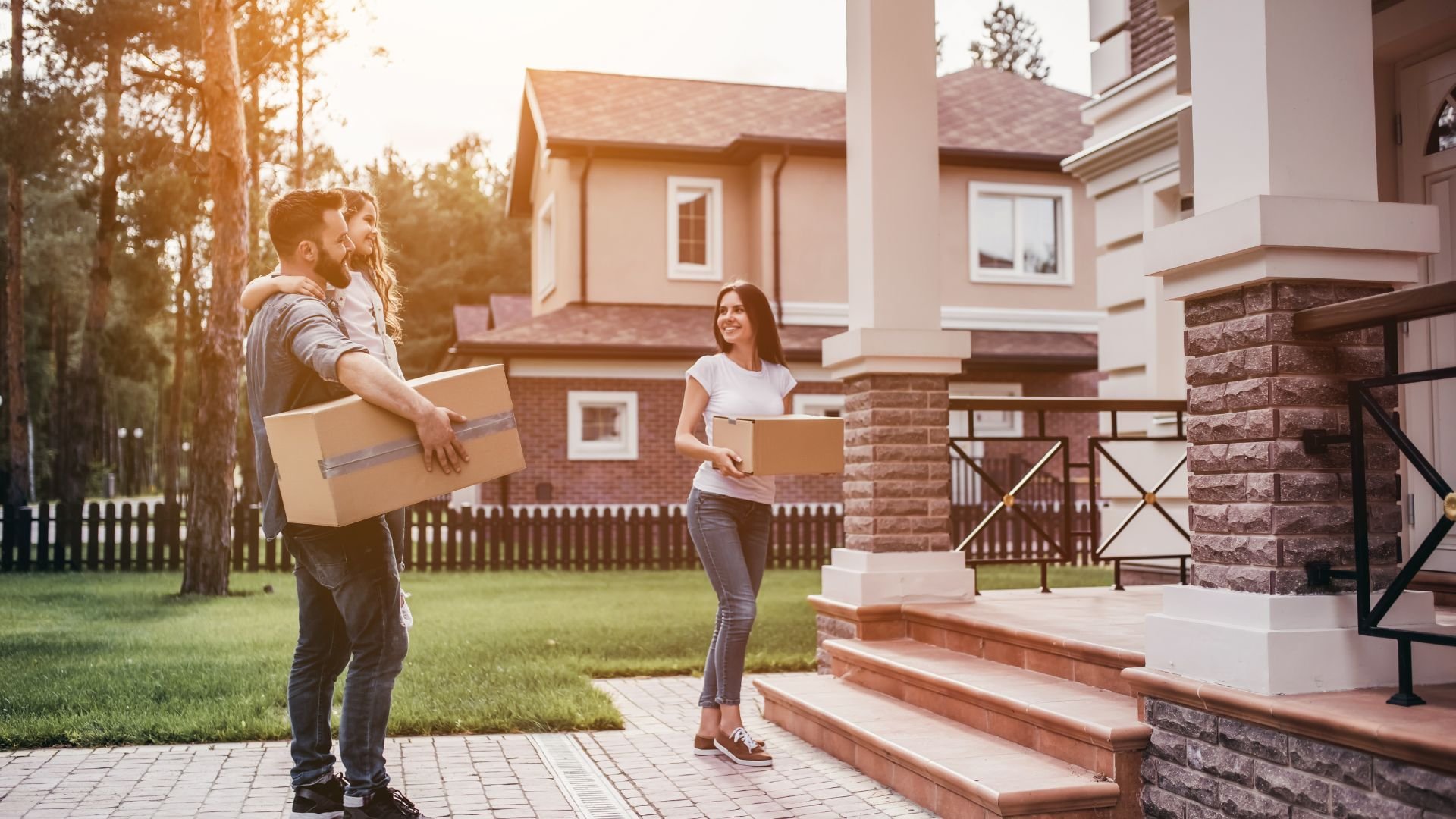 Couple carrying moving boxes in front of their new home at sunset